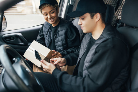 Two couriers in uniform sitting in a van checking delivery information on a digital tablet