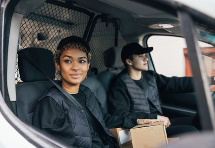 Two delivery coworkers in uniform sitting together in a van  Woman courier looking out from the window car while the man driving