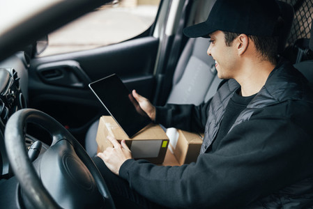 Close up of male courier sitting on a drivers seat checking delivery information on a digital tablet