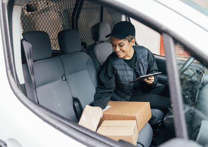 Smiling woman sitting on drivers seat checking packages and holding a digital tablet