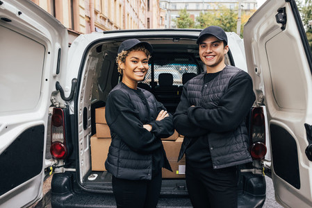 Portrait of a two confident and smiling couriers standing together at van trunk