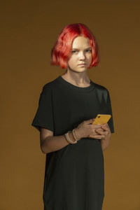 Portrait serious teenage girl with dyed red hair holding smart phone