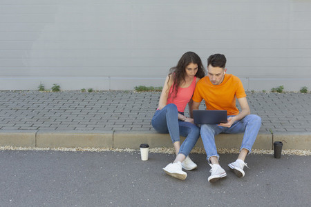 Young couple using laptop on curb