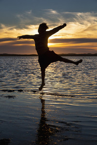 Silhouette boy jumping in ocean surf at sunset