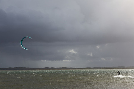 Kite boarder on ocean below stormy cloudy sky