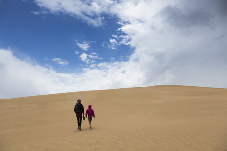 Mother and son walking along remote sand dunes