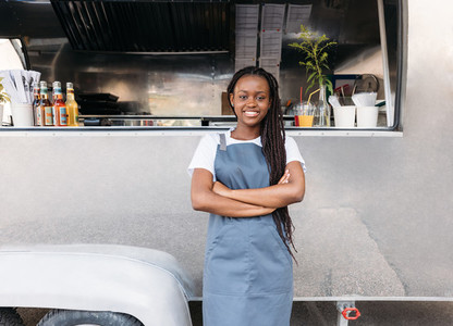 Young female waitress with long braids standing at food truck wearing apron