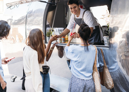 Smiling salesman giving beverages to customers while standing in food truck