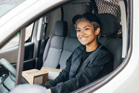 Portrait of a smiling woman working for delivery company sitting in a car looking away