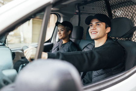 Two delivery coworkers sitting in van  Smiling courier driving a car
