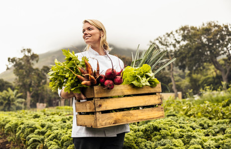 Thoughtful female chef carrying fresh vegetables on a farm