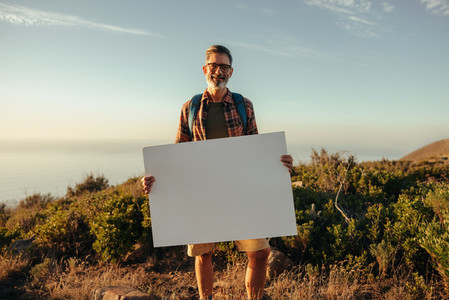 Hiker holding a blank placard on a hilltop