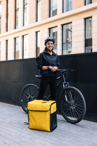 Portrait of a delivery woman standing in the city with bicycle and thermal backpack
