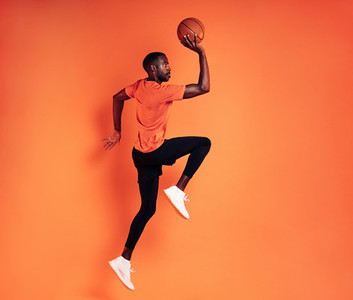 Side view of a sportsman with basket ball exercising against orange background