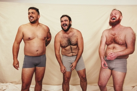 Three shirtless men laughing in a studio
