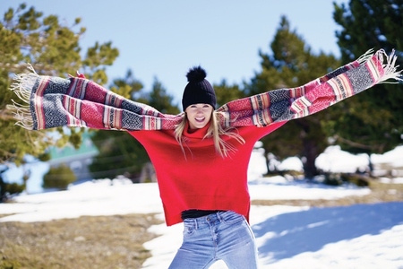 Happy young blonde woman waving her scarf in the wind in a forest in the snowy mountains