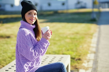 Female student taking a coffee break sitting on a bench outside her college