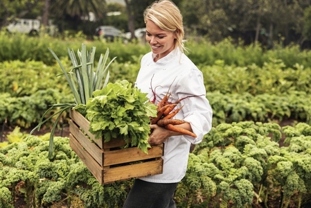 Smiling young chef carrying fresh vegetables on a farm