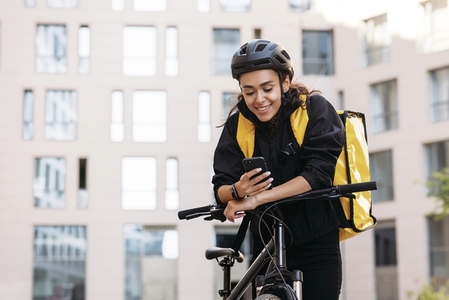 Portrait of a beautiful delivery girl holding her mobile phone while leaning on a handlebar of a bicycle