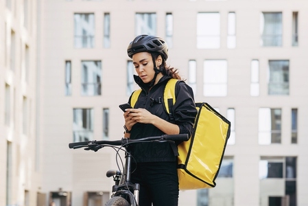 Woman courier with backpack checking information for delivery in the city