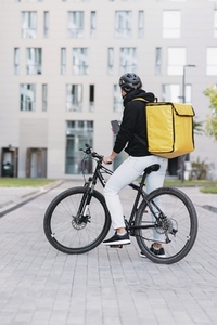 Back view of male courier with a thermal backpack with bicycle standing in the city