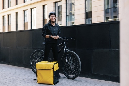 Happy woman in uniform standing in the city with bicycle and thermal backpack