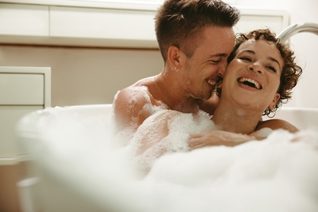 Playful queer couple having fun in the bathtub at home