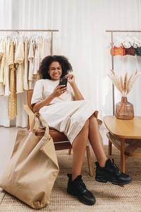 Smiling woman with mobile phone sitting on armchair in a clothing store  Customer relaxing in a boutique