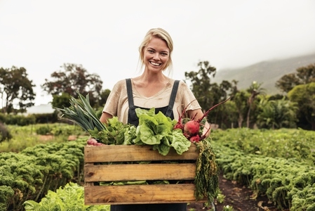 Cheerful organic farmer holding a box full of fresh produce on her farm