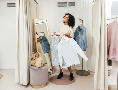 Smiling woman with clothes on hangers having fun in a dressing room