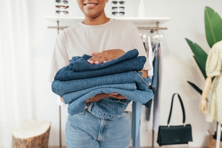 Close up of saleswoman carrying clothing in a small retail store  Cropped shot of female holding a pile of jeans