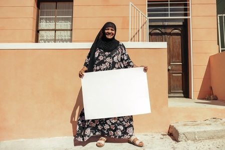 Happy Muslim woman holding a white placard outside her home