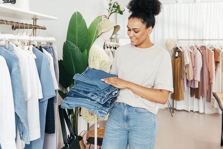 Young woman working in clothing store holding a pile of jeans