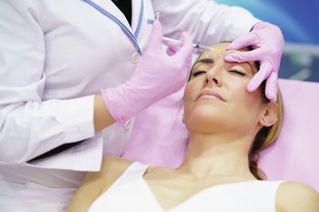 Aesthetic doctor injecting botulinum toxin into the forehead of her middle aged patient
