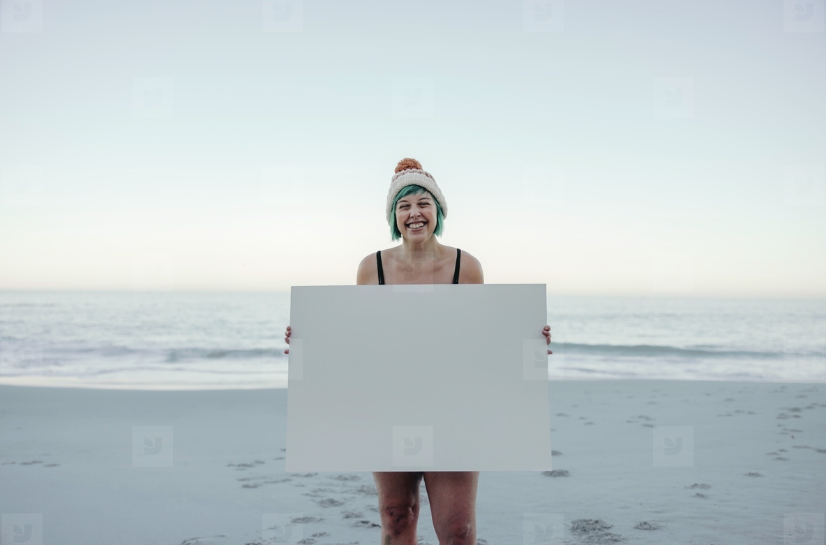 Self-confident winter bather holding a blan placard at the beach