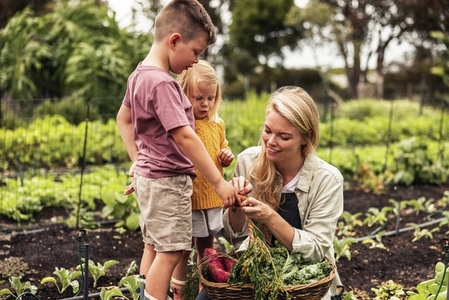 Cheerful young mother gathering fresh vegetables with her children