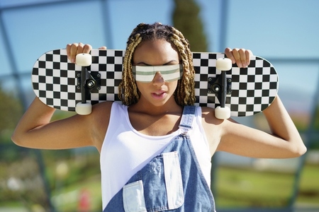 Black female dressed casual  looking at camera with modern sunglasses and an skateboard
