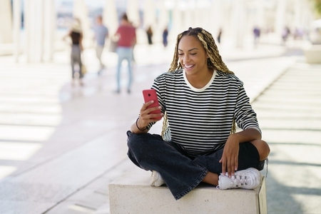 Happy black woman using a smartphone outdoors  wearing her hair in braids