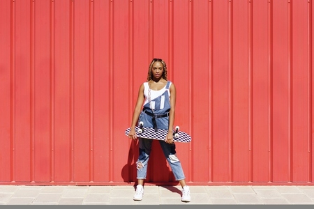Black woman dressed casual  wtih a skateboard on red urban wall background