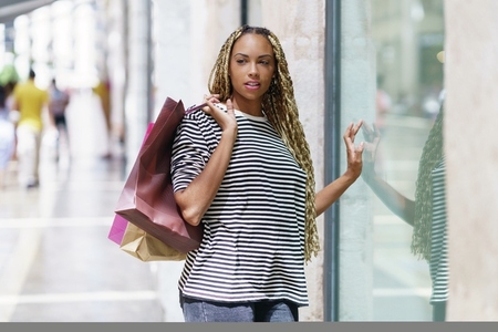Black woman in front of a shop window in a shopping street Female with african braids