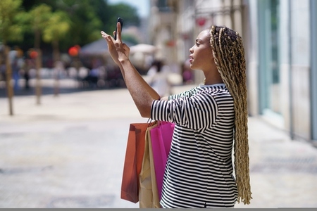 Black girl photographing something in a shopping street with her smartphone