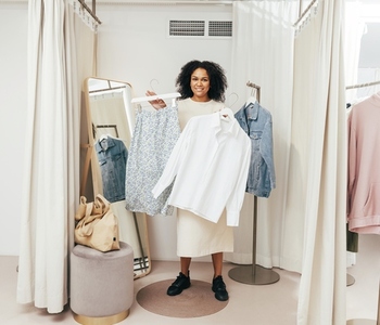 Stylish woman in fitting room standing with hangers looking at camera