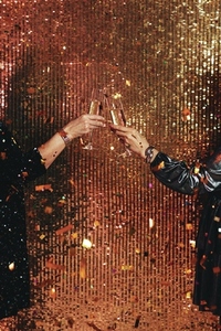 Hands of two mature women holding champagne glasses  Female toasting with champagne glasses against glitter background under confetti