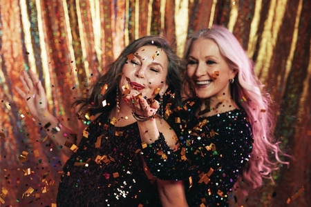 Two senior girlfriends having fun in studio blowing confetti
