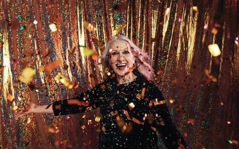 Stylish senior woman in black dress throwing confetti against a golden backdrop