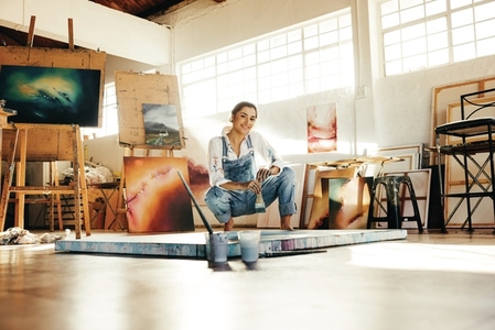 Cheerful young artist squatting close to her painting