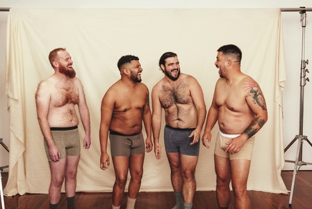 Four shirtless men laughing cheerfully in a studio