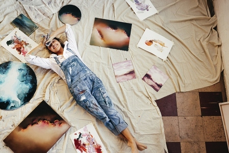 Overhead view of a painter lying in the middle of her paintings