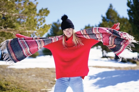 Young happy young blonde woman waving her scarf in the wind in a forest in the snowy mountains