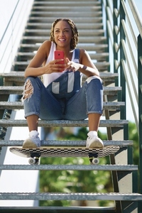 Black girl with coloured braids  sitting with a smartphone and a skateboard